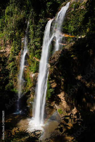 View of a high waterfall with sunlight and surrounded by rainforest