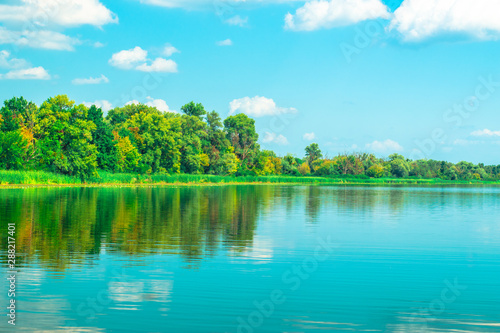 Landscape of a blue lake with reeds and green trees