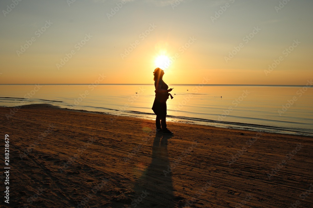 Beautiful sunset on the shore of the calm Gulf of Riga and the silhouette of a woman. June 2019. Latvia