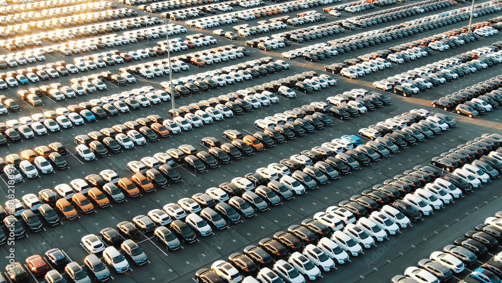 multicolored cars on warehouse parking lot lit by sunset - obrazy, fototapety, plakaty 