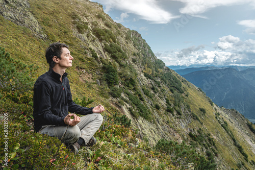 Man hiker sitting in a yoga pose at the peak of the mountain in the summer. Meditation after a long climb on a mountain © Artem