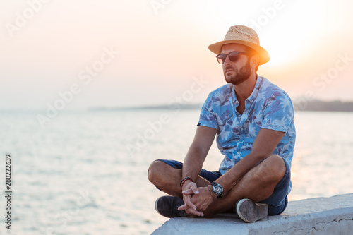 Young bearded man sitting by the sea in sunset