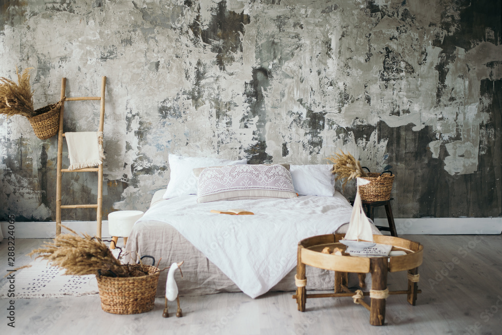Fototapeta obszar do sesji zdjęciowej w stylu loftu w jasnych kolorach. Stylowe, nowoczesne łóżko z detalami wnętrza z teksturowaną szarą ścianą. styl boho