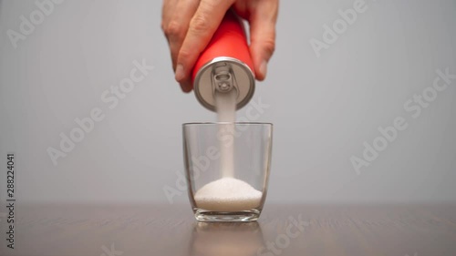 Close-up demonstration video of a man filling glass with sugar from red soda can. Sugar in soft drinks and sodas. Isolated, on white background
