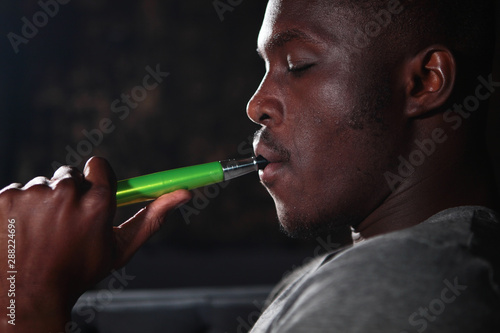 African American smokes a hookah. Portrait on a black background. The concept of smoking mixtures. Bad habits. © Alla