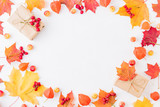 Flat lay frame with colorful autumn leaves and gift box on a white background