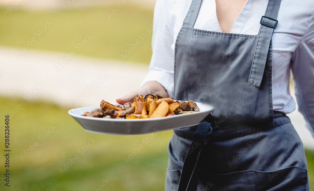 Catering service. Waiter man in apron carries food snacks on platter