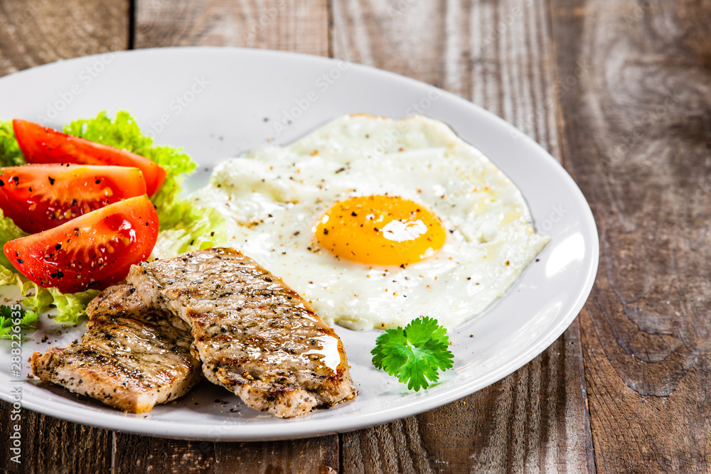 Grilled steaks with fried egg and vegetables on white plate Grilled steaks with fried egg and vegetables on white plate