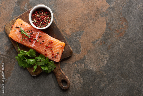 top view of raw fresh salmon with peppercorns, parsley on wooden cutting board