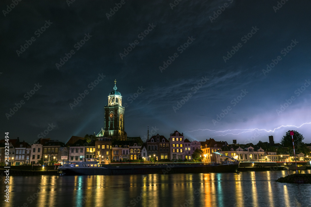 Beautiful view of the city of Deventer, the Netherlands at night with colorful reflections in the water of the river IJssel. Lightning bolt above the skyline of the city.