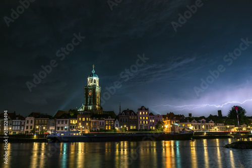 Beautiful view of the city of Deventer, the Netherlands at night with colorful reflections in the water of the river IJssel. Lightning bolt above the skyline of the city.