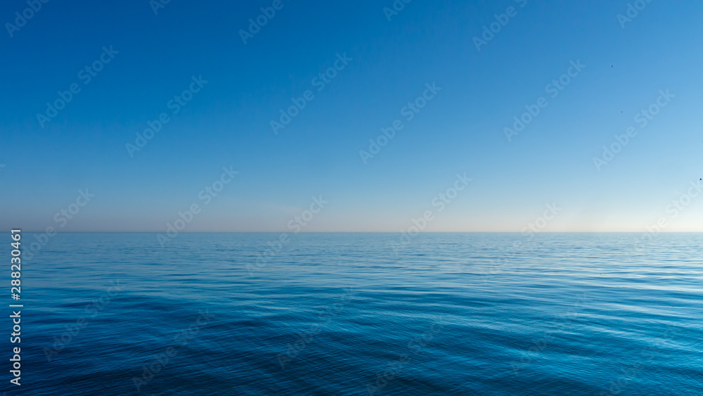 Obraz premium Relaxing/calming waves of the North Sea/Ocean taken during a warm sunny morning with a blue cloudless sky at Roker Pier, Sunderland, Tyne and Wear, England UK.