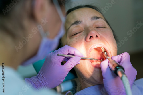 Dentist and patient in dentist office. Close-up of dental drill use for patient teeth in dentistry office in a dental treatment procedure. Woman having teeth examined at dentists