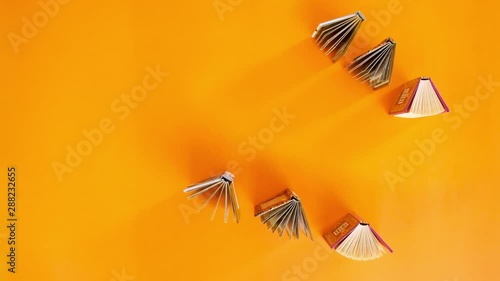 Stop motion animation of small paper books which run through an orange background with copy space. 4k education and back to school concept