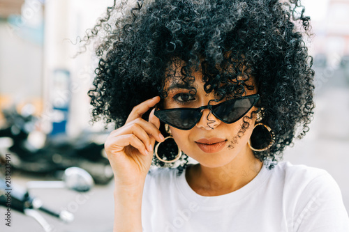 Pretty ethnic woman in white t-shirt and with black curly hair looking at camera over black glasses photo