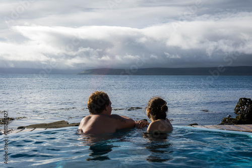 Couple bathing in Dragnsnes hot pots in the Westfjords region in Iceland looking at the ocean