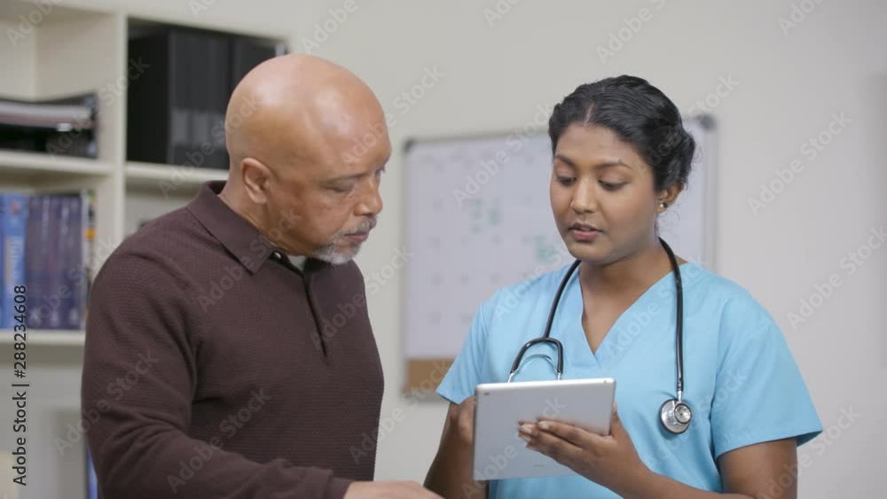 Nurse w/ stethoscope reviews info on tablet at nursing station, camera move left Nurse w/ stethoscope reviews info on tablet at nursing station, camera move left