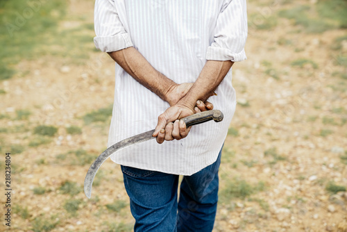 Rear view of farmer holding sickle in field photo