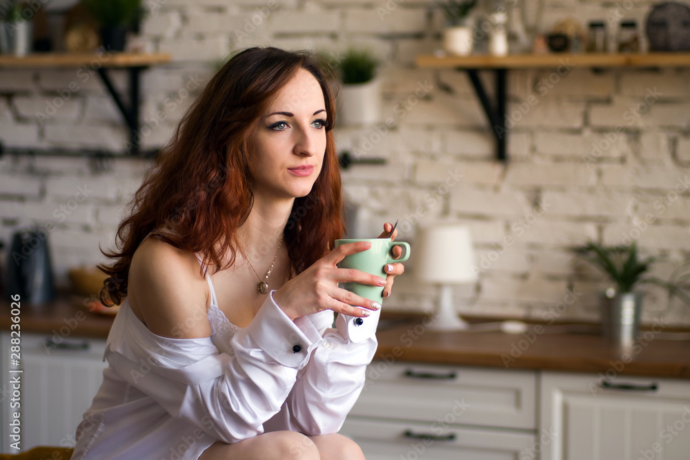 Adorable nice charming cheerful pretty trendy stylish girl drinking coffee, sitting on table countertop in modern light white kitchen Adorable nice charming cheerful pretty trendy stylish girl drinking coffee, sitting on table countertop in modern light white kitchen