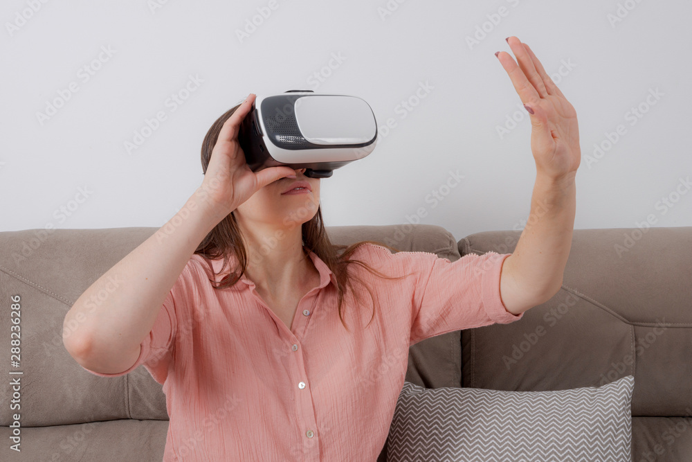 Woman using VR sitting on couch holding handset with one hand having the sensation of touching some virtual object. Woman using VR sitting on couch holding handset with one hand having the sensation of touching some virtual object.