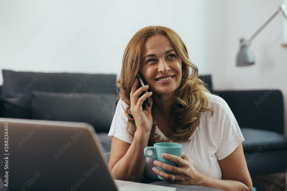mid aged woman using laptop computer while talking on mobile phone at her home mid aged woman using laptop computer while talking on mobile phone at her home