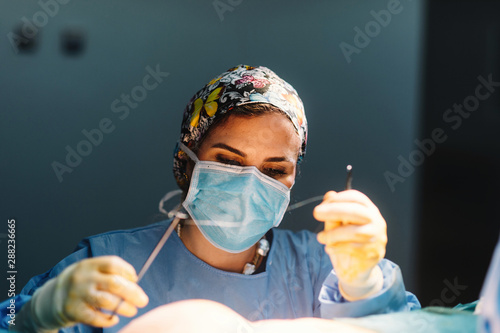 Plastic surgeon sewing up breast of female patient after inserting implants in operating room