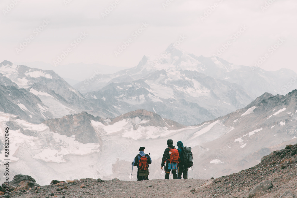 Extreme recreation and mountain tourism. A group of hikers down the mountain path over the horizon. In the background, large snow-capped mountains. Copy space.