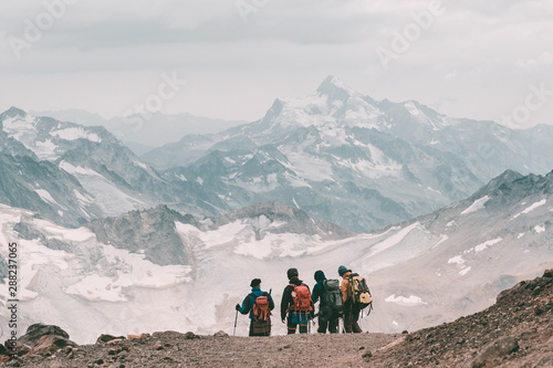 Extreme recreation and mountain tourism. A group of hikers down the mountain path over the horizon. In the background, large snow-capped mountains. Copy space