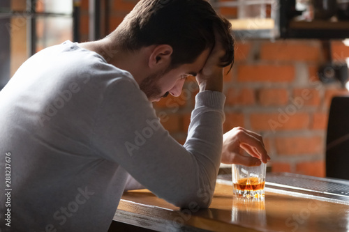 Obraz na płótnie Frustrated man sitting alone with glass of whiskey in bar