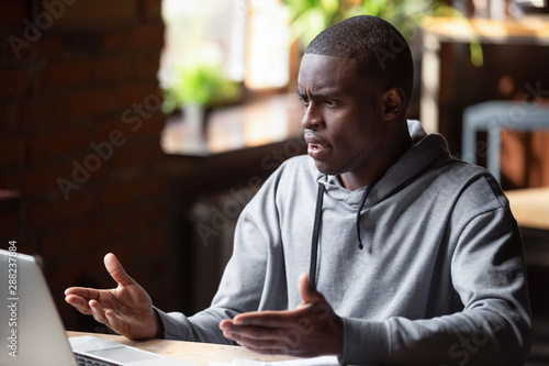 Angry African American man looking at laptop, receiving bad news