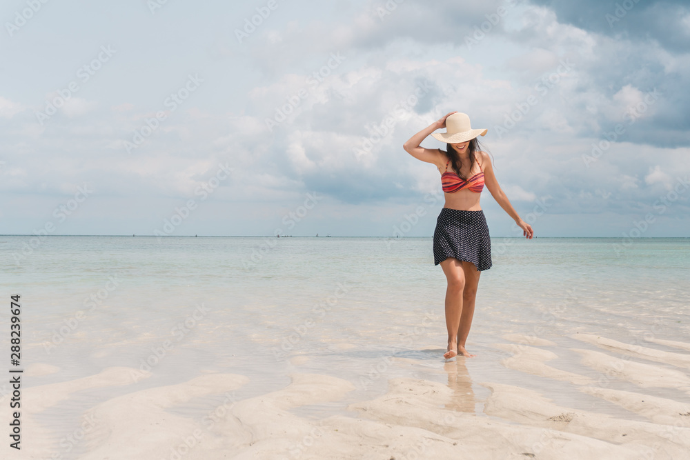 NUNGWI, Zanzibar, Tanzania: woman wearing a sun hat walking on the beach with low tide. 