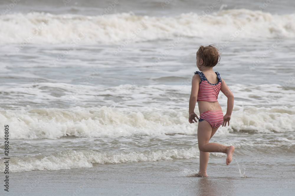 Little girl running toward ocean waves on the beach Little girl running toward ocean waves on the beach