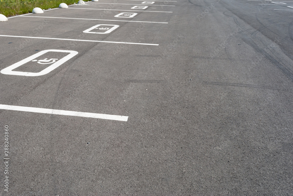 White disabled sign on a empty parking lot. Black tarmac texture with road marking 