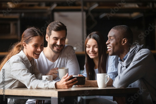 Happy diverse friends watching funny video on phone in cafe together