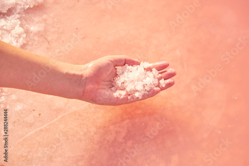 Woman's hand holding heap of salt in pink water photo