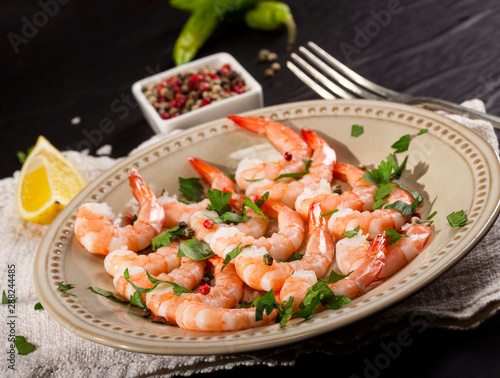 Prawns Shrimps on a plate with lemon, garlic and herbs on black background.