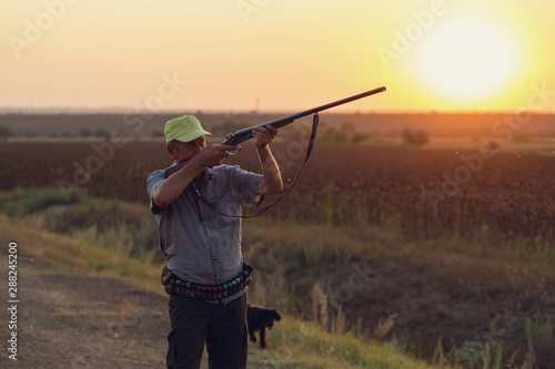 Hunting period, autumn season open. A hunter with a gun in his hands in hunting clothes in the autumn forest in search of a trophy. A man stands with weapons and hunting dogs tracking down the game.  © Mountains Hunter