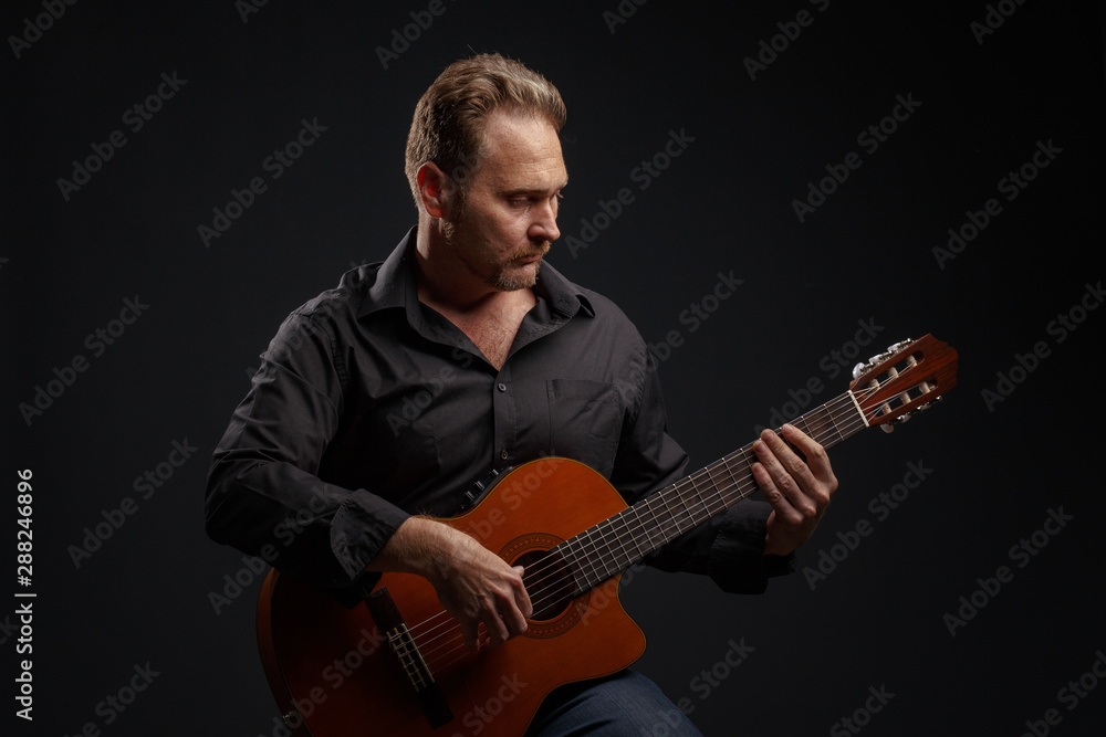 Obraz premium Man in black clothes plays a classic acoustic guitar. Studio photography.