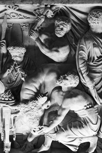 Black and white photo of old carved sculptures on marble showing animal sacrifice scene in an ancient roman party
