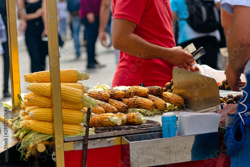 Street vendor prepares roasted chestnuts and corn on cobs on his street vendor cart.