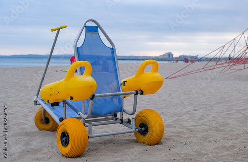 Beach wheel chair for disabled swimmers in the beach on blue sky and sea background. Concept of access to sea bathing and swimming for the disabled and people with reduced mobility. Summer vacation.