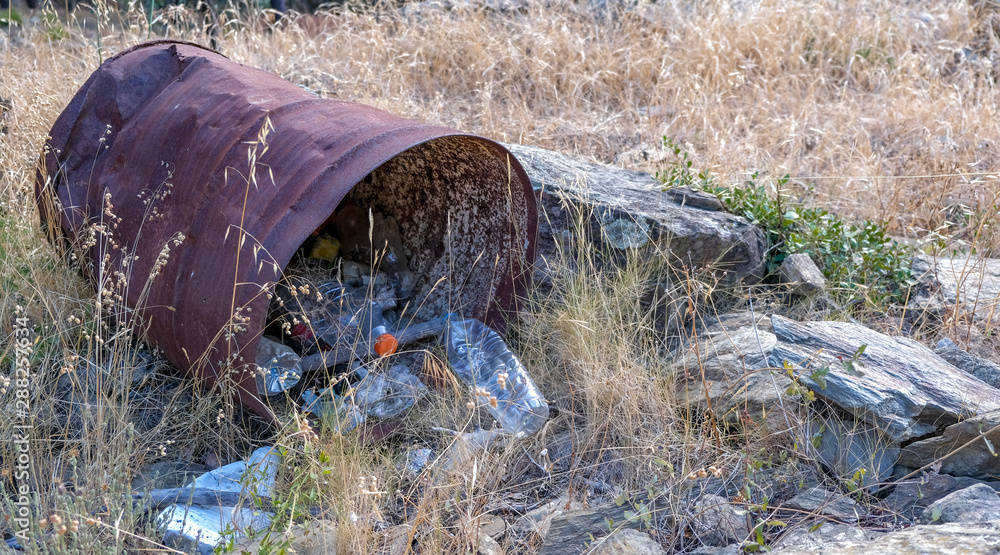 Obraz premium Large rusty iron barrel with plastic trash inside. Garbage in the forest. Environmental pollution by plastic. Bottles, cans in the dry grass. Global problem of Earth. 