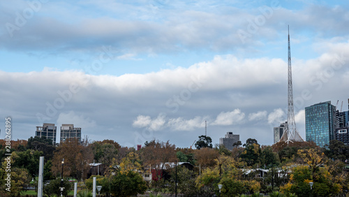 View of tower of Melbourne Art Centre from the park, clouds and blue sky, foliage and some buildings.