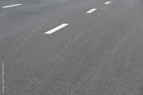 Low angle perspective view of two white paint dashed lines on asphalt road