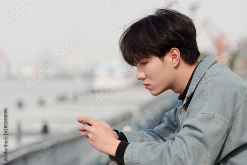 Portrait of a handsome Chinese young man holding his mobile phone, looking for something interesting in internet or playing games, mobile phone and the internet take up a lot of teenager's time.