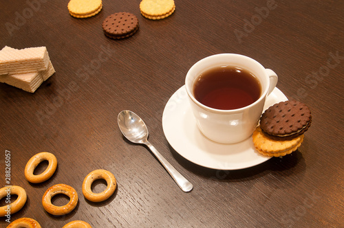 black tea in a white cup on a saucer with a spoon, with cookies and bagels on a dark wooden table