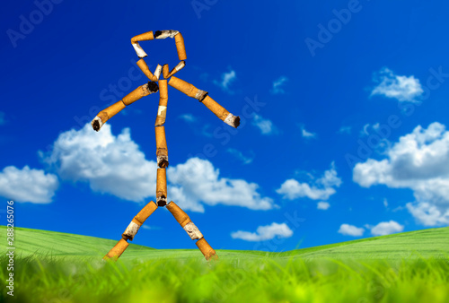 conceptual stick man of cigarette butts on green grass landscape over sunny sky
