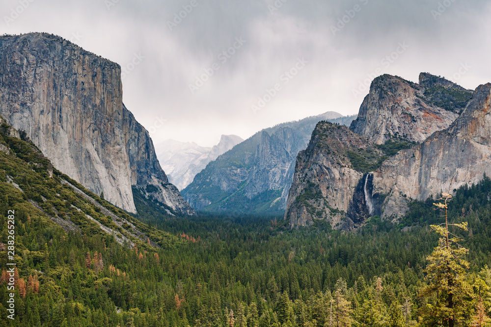 Yosemite National Park vista view of El Capitan, Half Dome, and Bridal Veil waterfall on cloudy day with rain falling Yosemite National Park vista view of El Capitan, Half Dome, and Bridal Veil waterfall on cloudy day with rain falling