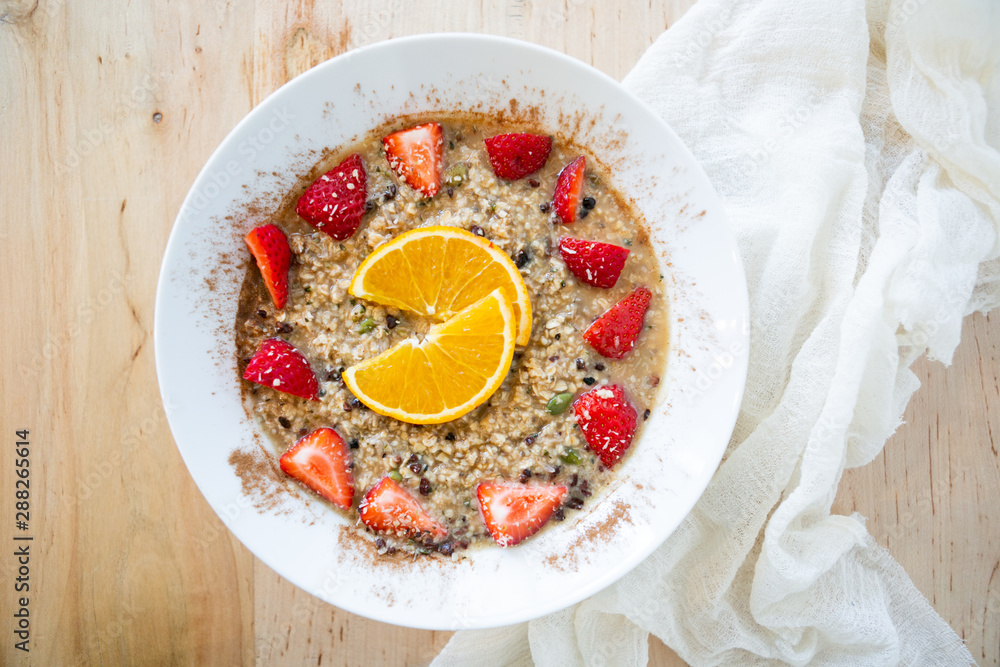 Superfood breakfast oatmeal bowl with fresh strawberries, orange slices, and maple syrup, on wooden table, linen napkin, modern tile, top view Superfood breakfast oatmeal bowl with fresh strawberries, orange slices, and maple syrup, on wooden table, linen napkin, modern tile, top view