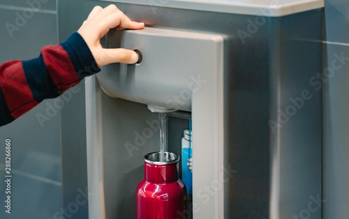 Hand of a traveler pressed the button of drinking water filling station at the Airport, fill up the reusable water bottle.  Eco friendly, Environmental awareness, No Plastic, Clean water, Zero waste.